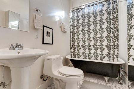 Charming bathroom w/ a clawfoot tub, bold printed curtain & pedestal sink.