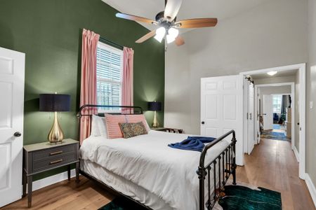 Airy bedroom w/ green walls, a ceiling fan & natural light streaming in.
