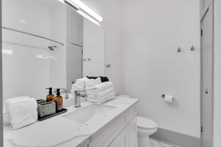 Modern bathroom w/ marble vanity, tub & shower combo, & neatly folded towels.