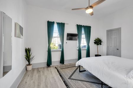 Bright bedroom w/ teal drapes, a/c unit, & a lush plant for a fresh, airy feel.