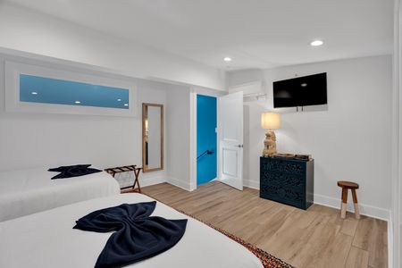 Bedroom 2 w/ a teal door, wall-mounted TV & warm wood floors for a cozy retreat.