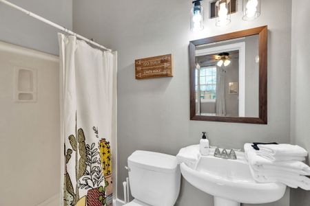 Bright bathroom w/ a tub, wood-framed mirror & bold floral curtain for a homey touch.