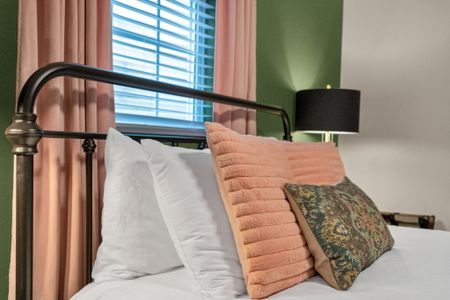 Bedroom w/ green walls, blush curtains & a bold patterned rug underfoot.