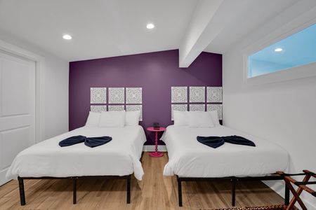 Bedroom 2 w/ twin beds, purple walls & warm wood floors for a cozy, stylish sleep.