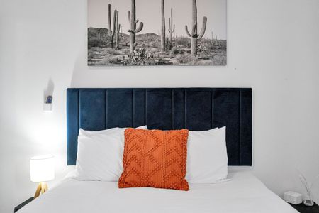 Bold bedroom w/ velvet navy headboard, orange pillows, & crisp white bedding.
