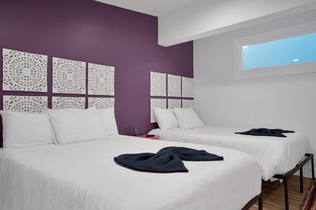 Bedroom 2 w/ plush white bedding & a dramatic purple accent wall for moody rest.