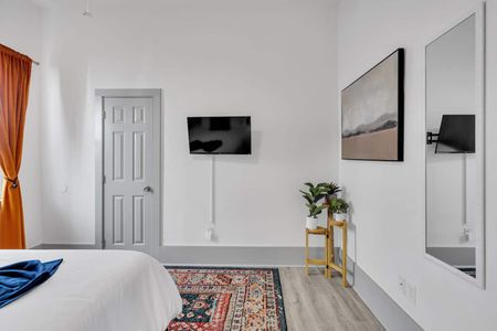 Bright bedroom w/ mounted TV, cozy bed, & soft lighting for a relaxing wind-down.