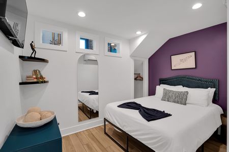 Bedroom 1 w/ crisp white bedding & rich purple accent wall for a moody, restful vibe.