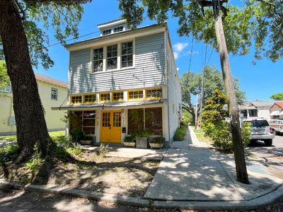 Charming exterior w/ lush greenery & a welcoming yellow front door.