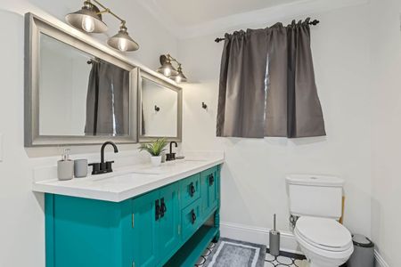 Bright bathroom w/ teal cabinets, a sink & well-lit mirror.
