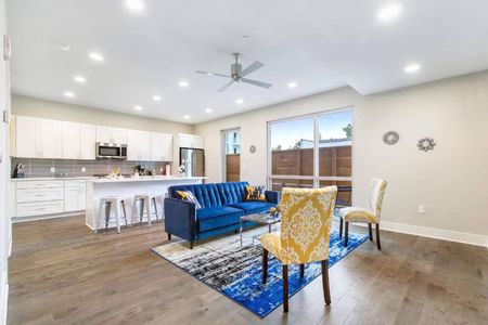 Airy living room w/ ceiling fan, blue sofa & dining nook bathed in natural light.