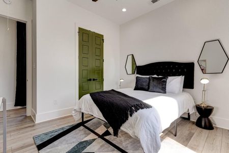 Bedroom w/ bold dark headboard, crisp white linens & a dramatic green door.