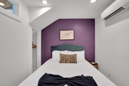 Bedroom 1 w/ a plush bed framed by a deep purple wall & soft, layered bedding.