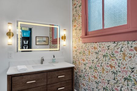 Warm, moody bathroom w/ backlit mirror & a sink w/ clean lines.