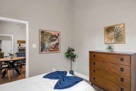 Sunlit corner w/ tropical artwork & a wood dresser — relaxed & full of character.