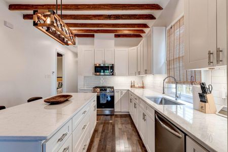 Clean white kitchen w/ exposed beams & modern fixtures for a polished, airy feel.