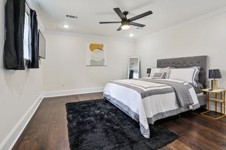Clean, bright bedroom w/ a centered bed, dark rug & ceiling fan overhead.