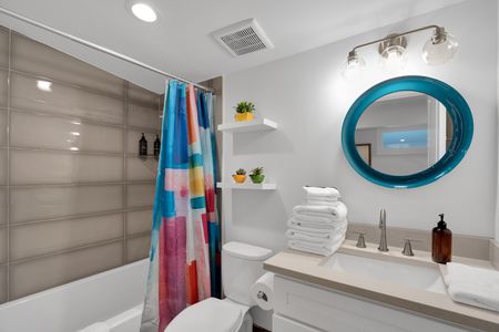 Bathroom 2 w/ a colorful shower curtain, teal mirror & neatly stacked fresh towels.