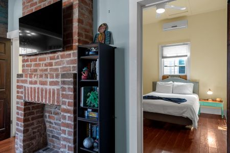 Sunlit bedroom corner w/ exposed brick & cozy, lived-in warmth.