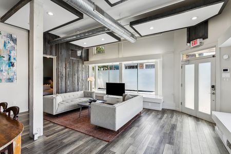 Bright living room w/ cozy sofa seating & a TV, framed by big windows.