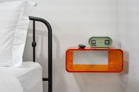 Bright orange floating nightstand & retro flip clock add a playful pop beside the classic iron bed