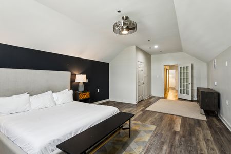 Moody bedroom w/ dark accent wall, bed & wood floors.