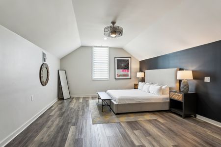 Vaulted-ceiling bedroom w/ bed & warm wood floors.