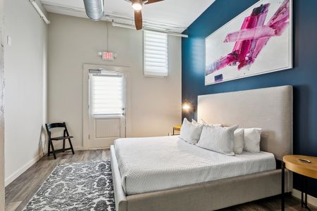 Bright bedroom w/ bed, colorful art & direct door access outside.