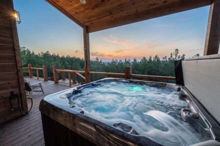 Private hot tub on a cabin deck overlooking a forest at sunset, offering a luxurious