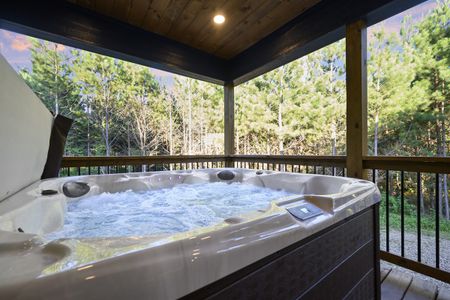 Outdoor hot tub on a cabin patio overlooking a lush forest landscape, providing a tranquil