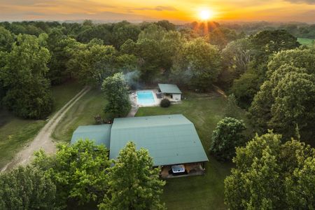 Aerial view of a cozy cabin and swimming pool nestled in a lush, green landscape