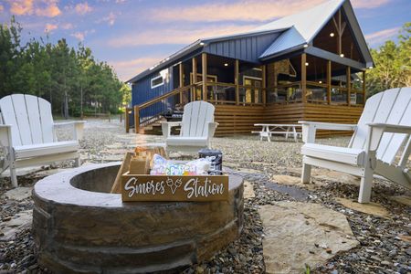 Luxury cabin exterior with outdoor patio, Adirondack chairs, fire pit, and "S'mores Station" sign, perfect