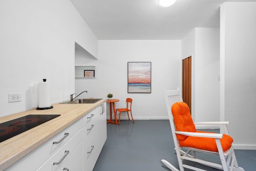 A sunny, stylish room with a blue accent wall, white rocking chairs, and a small table, featuring a world map and colorful artwork, creating a cozy and vibrant space.