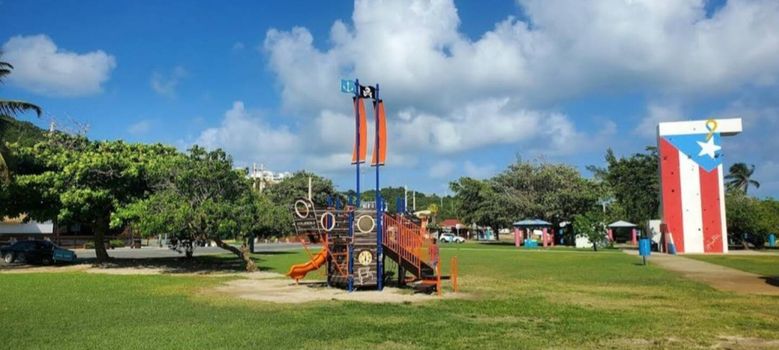 Family fun meets iconic landmarks! Enjoy this vibrant pirate-themed playground with the striking Puerto Rico flag monument in view.