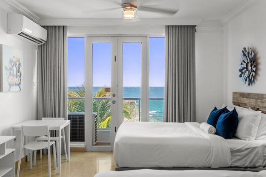 Indulge in the ultimate seaside escape in this spacious bedroom, offering two plush beds and floor-to-ceiling glass doors that open to stunning panoramic ocean vistas.