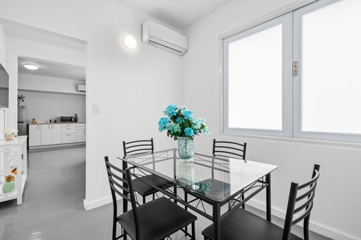 Indulge in urban elegance with our modern dining space, complete with a sleek glass table, chic black chairs, and a vibrant blue floral centerpiece.