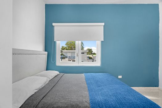 Experience relaxation in a minimalist space that combines comfort with clean lines and features a cozy bed, highlighted by a striking blue wall for a pop of color.