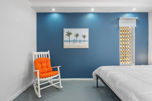 Enjoy a cozy, modern room with a bold blue accent wall, comfortable white rocking chairs, and contemporary decor, creating a vibrant yet relaxing space.