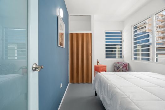 This spacious room features modern amenities and sleek design. The blue accent wall adds a pop of color to the space. A piece of modern artwork hangs on the blue wall adding an artistic touch to the room. A large window allows ample natural light to flood into space, enhancing its brightness.