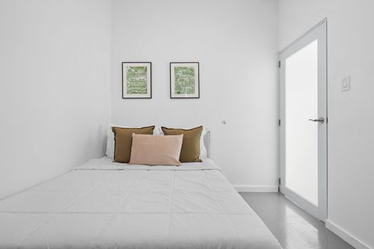 Relájese en esta elegante habitación con una cama bien hecha, paredes blancas y un toque de verde en obras de arte enmarcadas.