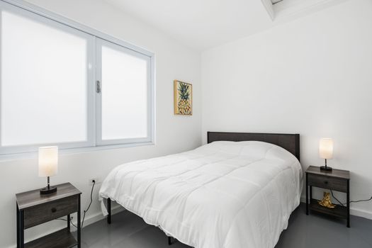 Un dormitorio sereno que cuenta con una lujosa cama tamaño queen adornada con sábanas blancas impecables, flanqueada por mesas de noche contemporáneas e iluminación ambiental, que ofrece un refugio tranquilo.