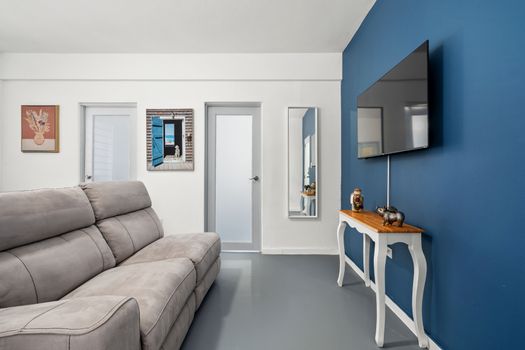 A stylish, colorful room with a blue accent wall, white rocking chairs, and a flat-screen TV, showcasing a world map and abstract art, creating a lively and cozy space.