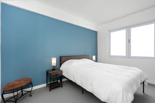 Disfrute de una noche de descanso en este moderno dormitorio que cuenta con una cómoda cama, acentuada por la relajante pared azul y la abundante luz natural que entra por el gran ventanal.