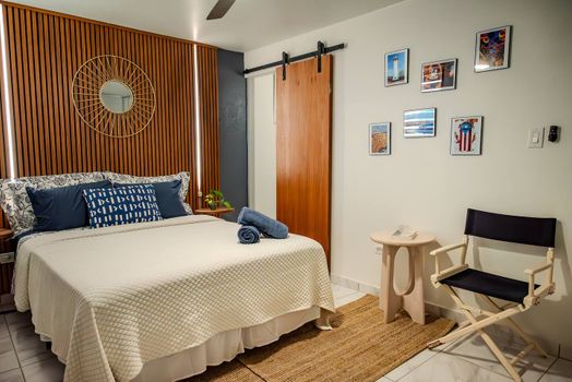 Indulge in modern comfort in this stylish bedroom featuring a striking slatted wooden accent wall with ambient lighting, a plush queen bed, and a unique barn door.