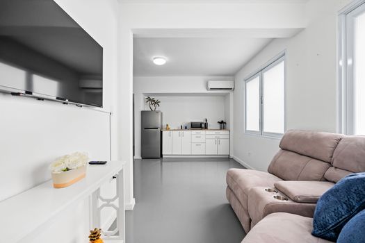 Our modern studio apartment offers a perfect blend of comfort and style, with a cozy beige sofa, chic white furnishings, and a fully-equipped kitchenette.