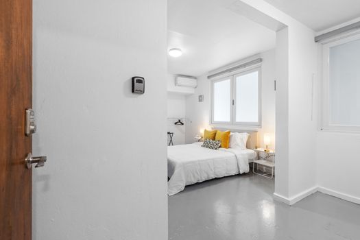Entrada amplia y luminosa a un dormitorio sencillo con paredes y ropa de cama blancas y limpias.