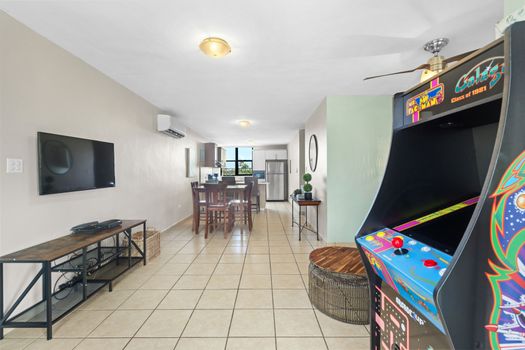Open-concept living area seamlessly connects to the dining space, featuring modern amenities and a touch of nostalgia with a classic arcade game.