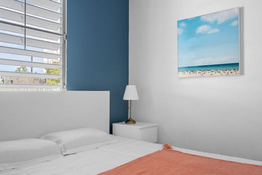 Elevate your stay with a peaceful night's sleep in this stylish bedroom adorned with minimalistic furniture and tranquil beach artwork.