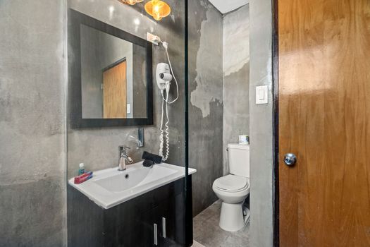 Step into this sleek bathroom featuring a polished concrete wall, contemporary fixtures, and warm wooden door accents.