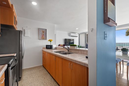 Kitchen space featuring light brown tiled counters, stainless steel double sink, and ample wood cabinets for storage.
